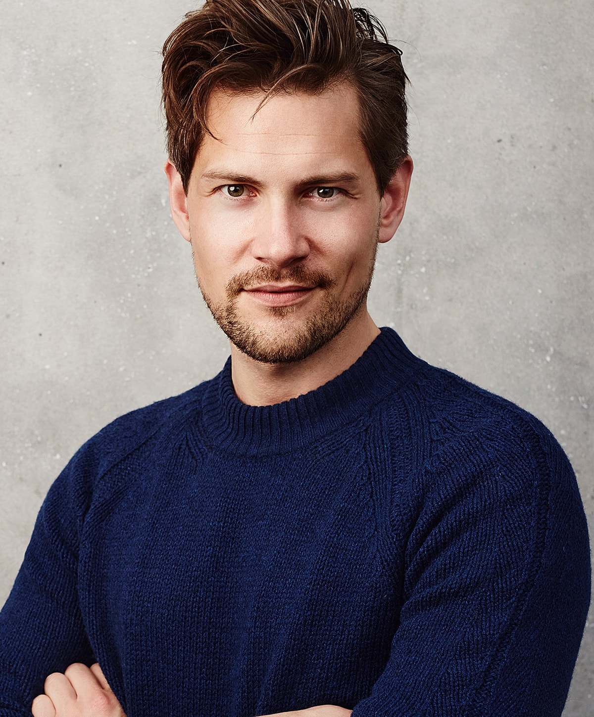 Smiling man in a blue sweater against textured background.