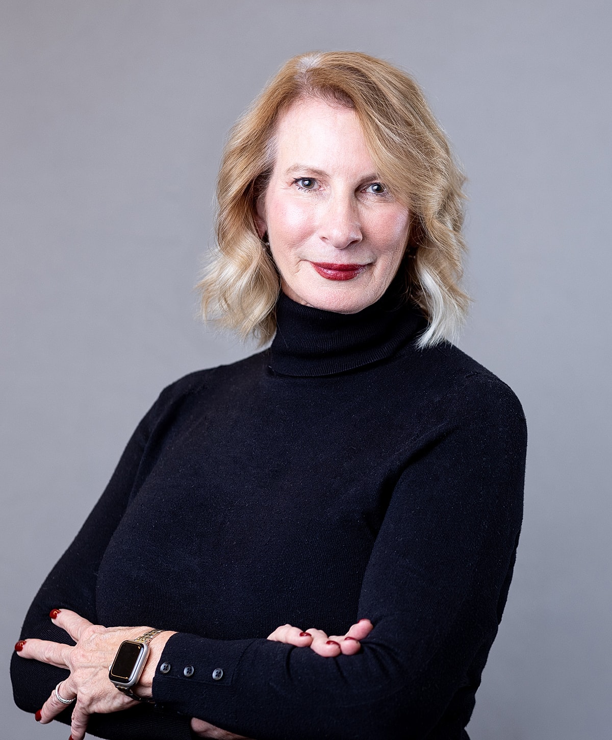 Woman in black turtleneck, arms crossed, smiling.