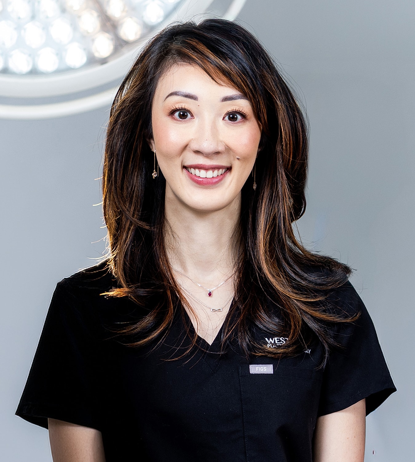 Smiling woman in medical scrubs against background light.