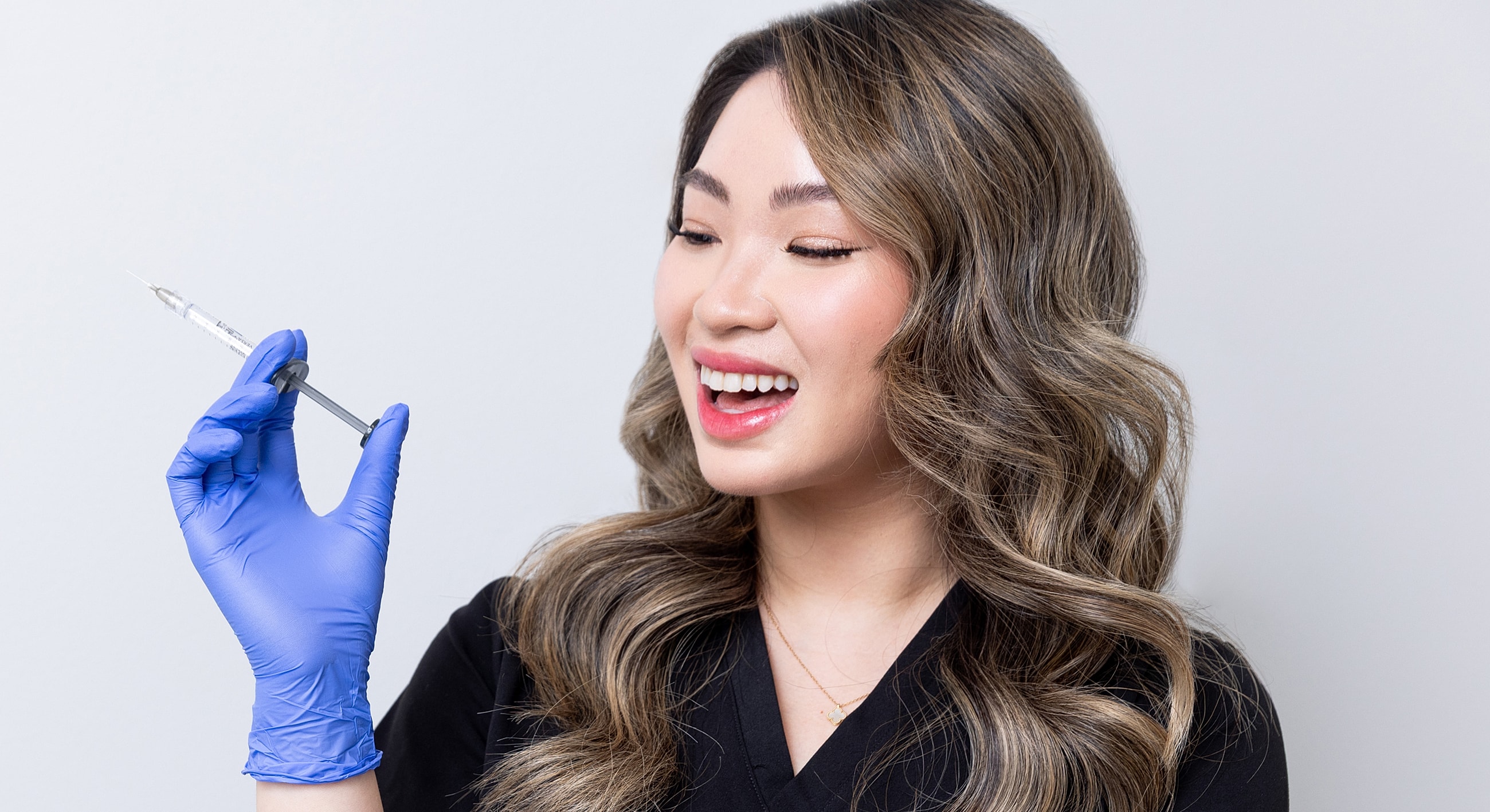 Smiling person holding a syringe in gloved hand.