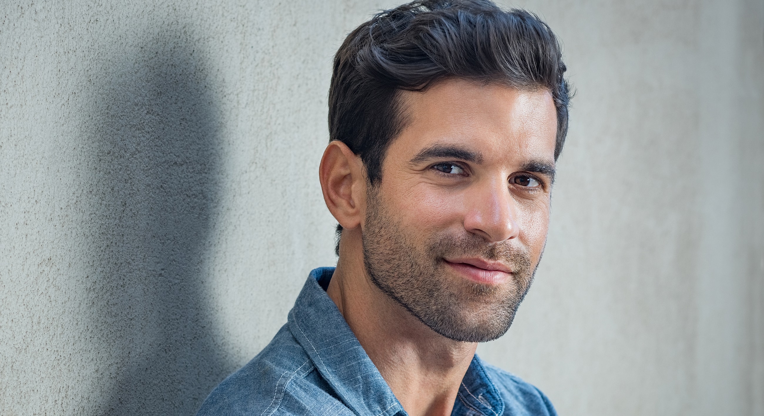 Man smiling against a textured wall background.