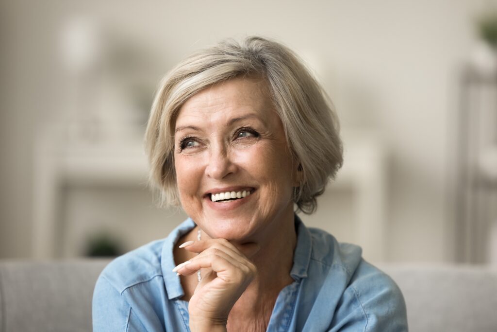 Older woman smiling and touching her chin to show off how her facelift has changed with age