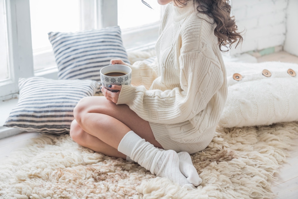 Woman drinking hot drink in cozy clothes indoor, recovering from mommy makeover.